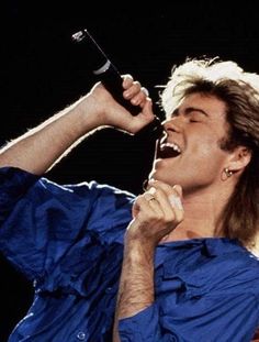 a man singing into a microphone while holding his hand up to his ear and wearing a blue shirt