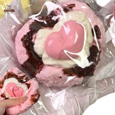 a person holding a pink and white pastry in plastic wrapper next to other pastries