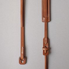 two leather straps hanging on the wall next to each other, one has a clasp