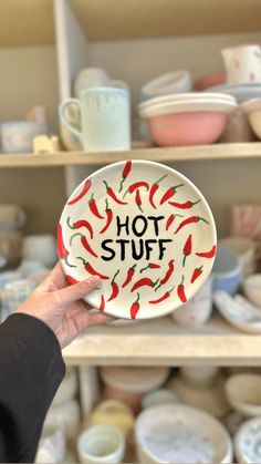 a person holding up a plate with the words hot stuff on it in front of shelves