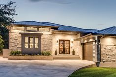 a modern home with stone and metal roofing in the evening light, lit up by street lights