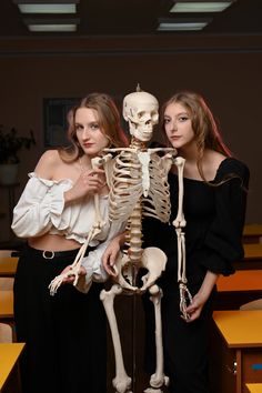 two young women standing next to each other with a skeleton in front of their backs