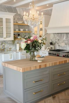 a kitchen island with flowers on it in front of a chandelier and cabinets