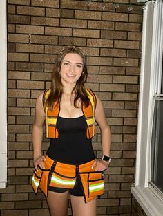 a woman in an orange safety vest standing next to a brick wall wearing reflective clothing