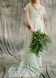 a woman in a white dress holding a green plant and looking at the camera while standing against a gray backdrop