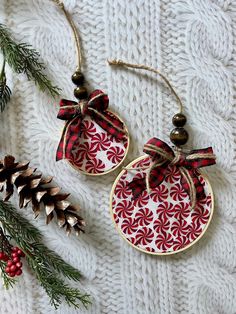 two red and white christmas ornaments hanging from twine with pine cones in the background