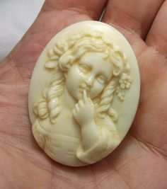 a hand holding a white carved stone with a woman's face on it, in front of a white background