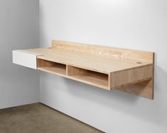 a wooden shelf on the wall with two open compartments below it, in an empty room