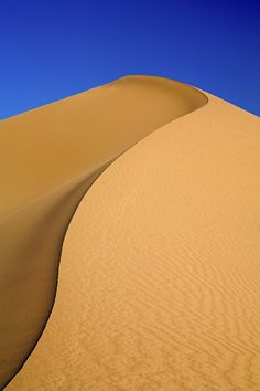 the sky is blue and there are no clouds in the desert, but it looks like sand dunes