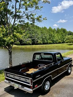 an old black truck parked next to a tree in front of a body of water