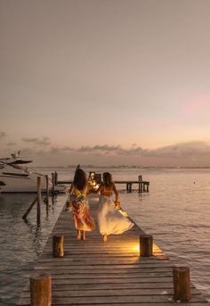 two girls are walking on a dock at sunset