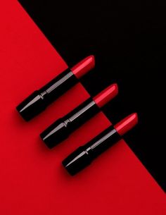 three red lipsticks on a black and red background