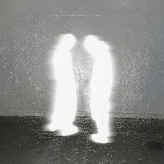 two people standing in front of a wall with light coming from their faces and arms