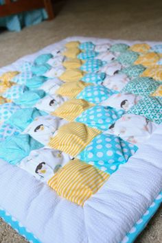 a baby quilt is laying on the floor in front of a crib with blue and yellow polka dots