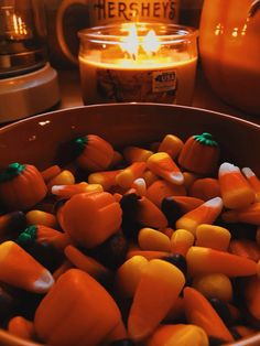 a bowl filled with candy corn next to a lit candle