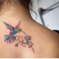 a colorful bird tattoo on the back of a woman's upper back neck and shoulder