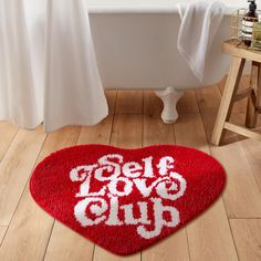 a red rug with the words self love club written on it in front of a bathtub