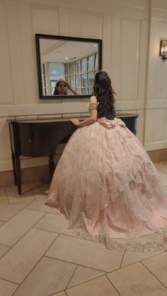 a woman in a pink dress is sitting at a piano and looking into the mirror