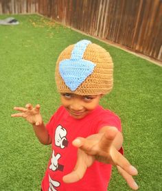 a young boy wearing a crocheted hat and making the peace sign with his hands