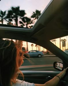 the woman is driving her car down the street at sunset or dawn, with palm trees in the background