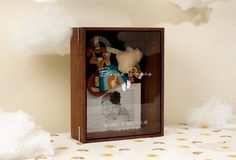 a stuffed animal in a wooden box on a bed with white fluffy clouds behind it