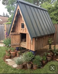 a small wooden house with a metal roof in the grass next to potted plants