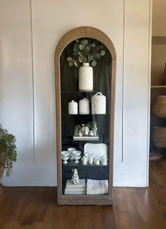 a display case filled with white items on top of a wooden floor next to a potted plant