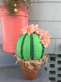 a potted plant with flowers and straw in front of a pink flowerpot on a porch