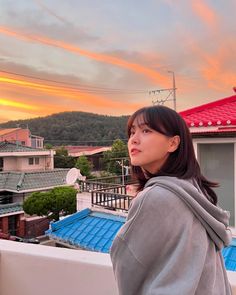 a woman standing on top of a roof next to a red and white building at sunset