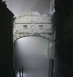 a bridge that is over some water in the foggy night with no people on it