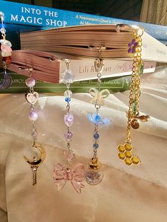 several charms hanging from a book on top of a white sheet with a pink bow