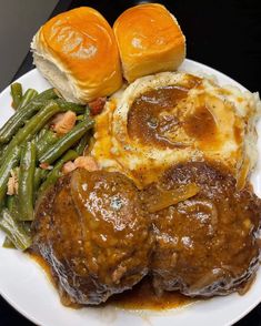 a white plate topped with meatballs, green beans and potatoes next to bread rolls