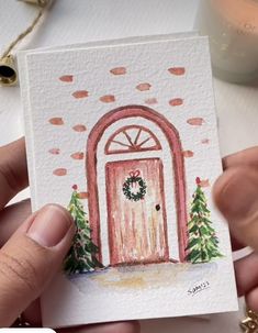 a hand holding up a card with a painting of a door and wreath on it