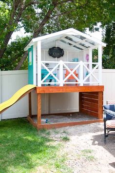 a play house with a slide in the back yard, and a tree behind it