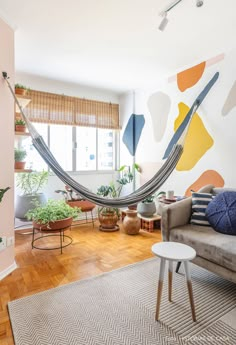 a hammock hanging in the middle of a living room with potted plants