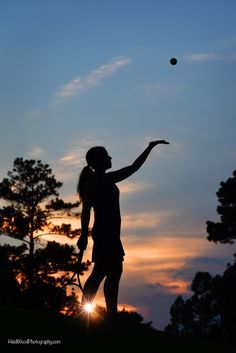 a woman holding a tennis racquet standing next to a tree with a ball in the air