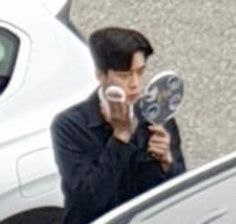 a man holding two mirrors in front of his face while standing next to a white car