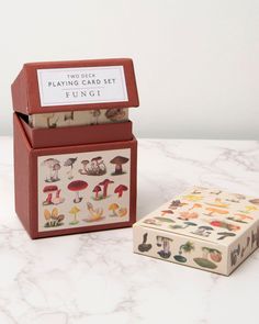 two boxes with different designs on them sitting on a table next to a box that says playing card set fungi