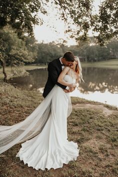 a bride and groom kissing in front of a lake