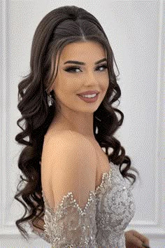 a woman with long dark hair wearing a silver dress and smiling at the camera while standing in front of a white wall