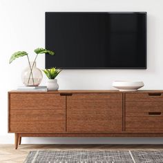 a large flat screen tv mounted on the wall above a wooden cabinet with two planters