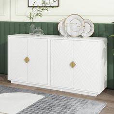 a white sideboard with two plates on top and a plant in the corner next to it