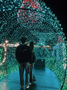 two people standing in front of a tunnel covered with lights