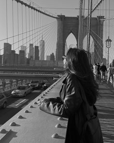 a woman standing on the side of a bridge looking at cars passing by in front of her