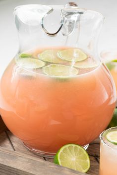 a pitcher filled with orange liquid and limes