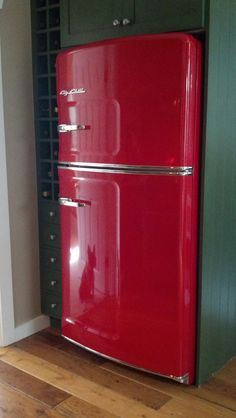 a red refrigerator sitting in the corner of a room next to a green cabinet and wooden floor