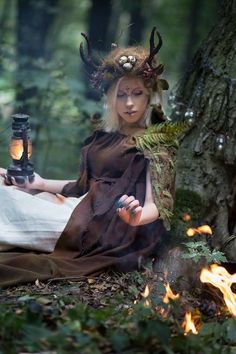 a woman sitting on the ground next to a tree with antlers in her hair