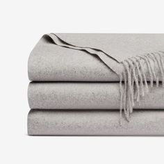 three folded sheets with fringes on them, one in grey and the other in white