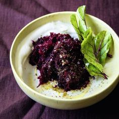 a white bowl filled with food sitting on top of a purple table cloth next to a green leafy plant