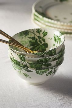 four green and white bowls with chopsticks in them sitting on a tablecloth